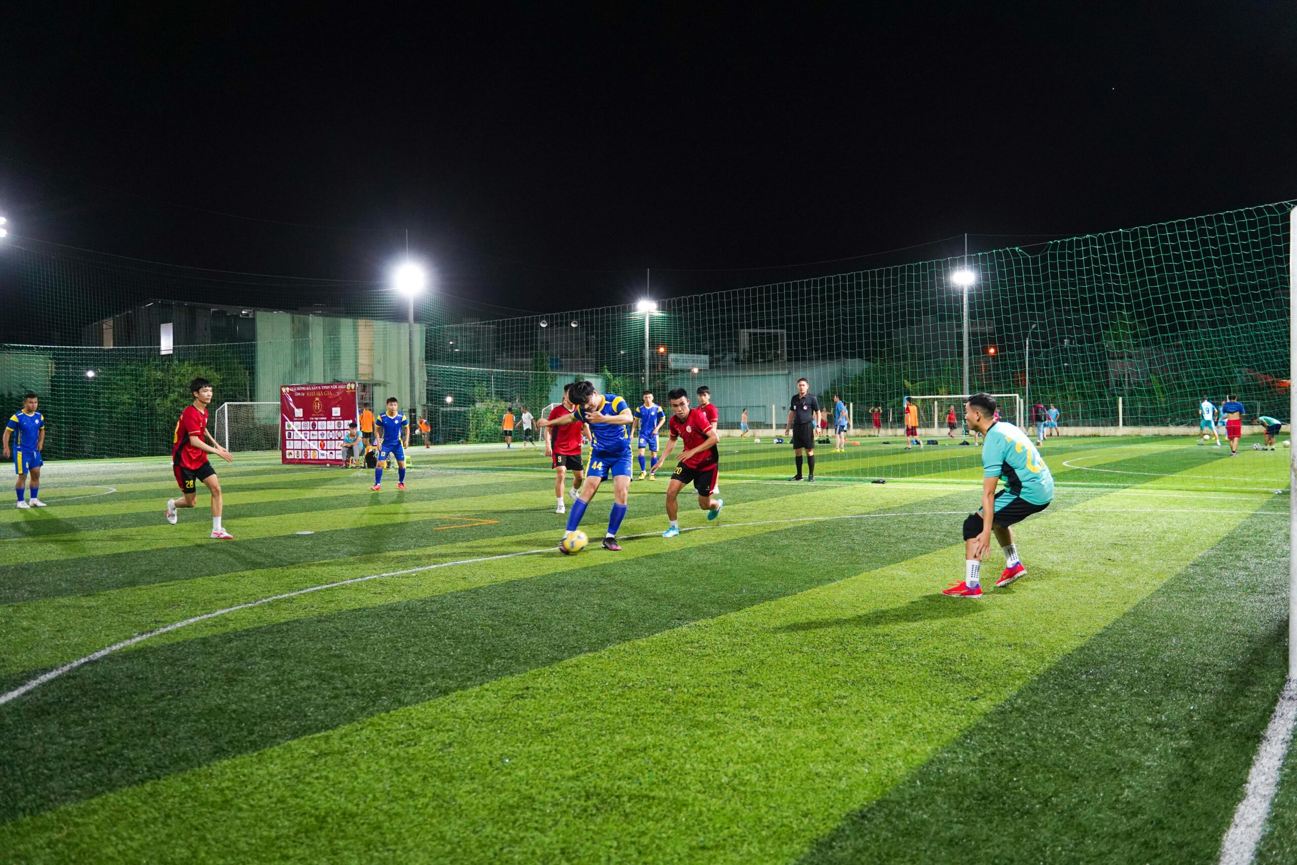 Young athletes playing a competitive soccer match on a lit artificial turf field at night.