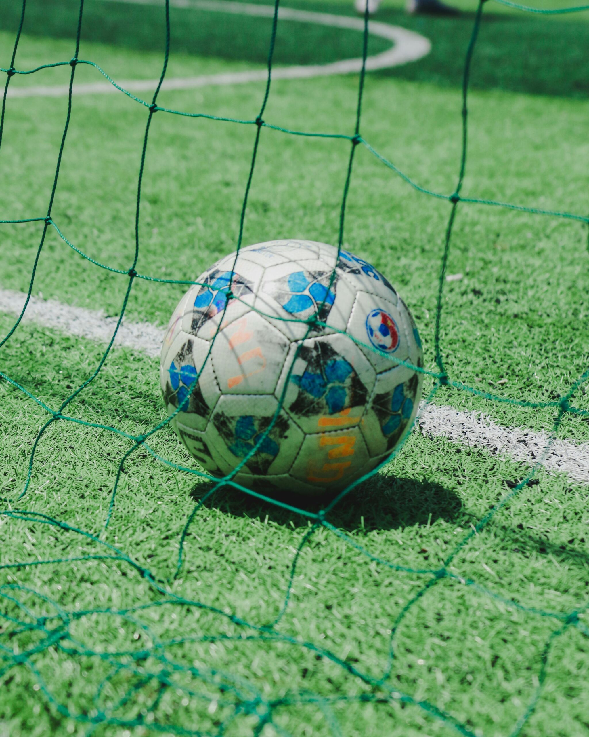 Close-up of a soccer ball resting on green turf with net, ideal for sports themes.